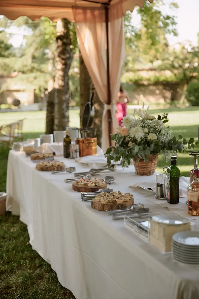 Tavola imperiale per il buffet di un matrimonio all'aperto con fiori e drappi in lino
