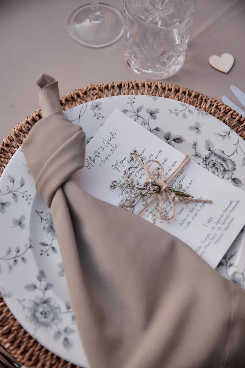 Mise en place con piatto fiorato, sottopiatto in rattan e menu personalizzato del matrimonio