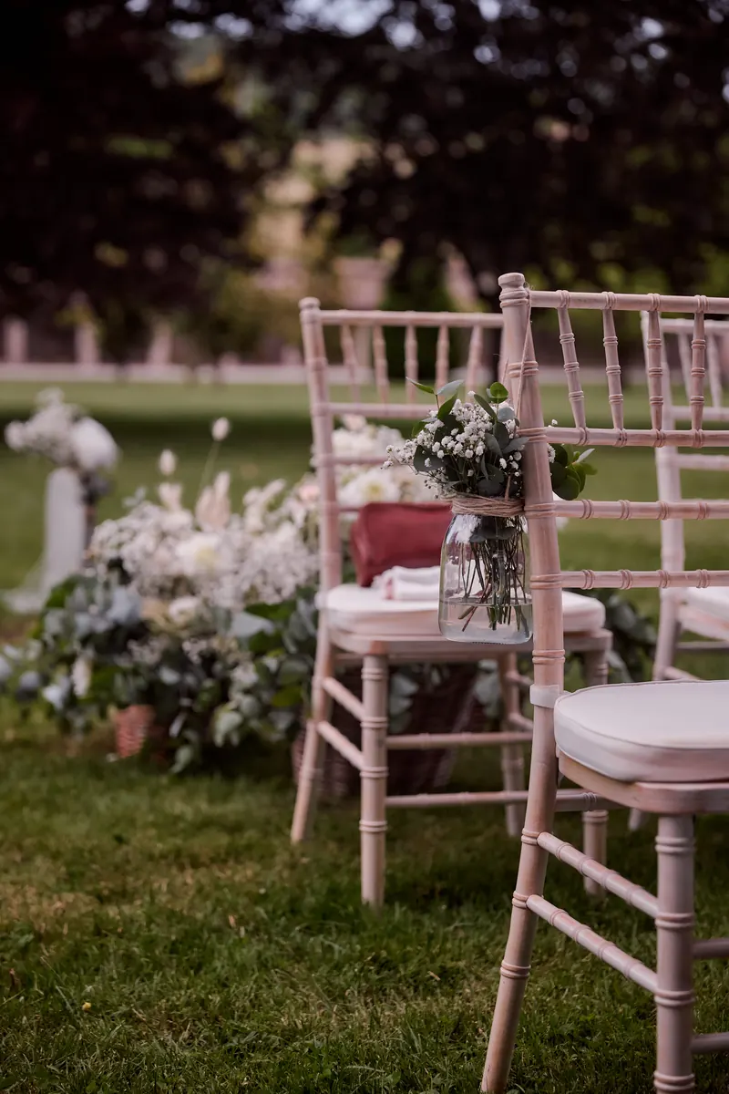 Sedie chiavari rosa cipria e composizioni floreali lungo la navata di una cerimonia all'aperto